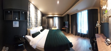 A hotel room with a bed, a desk, a chair, a TV, and a window with curtains.