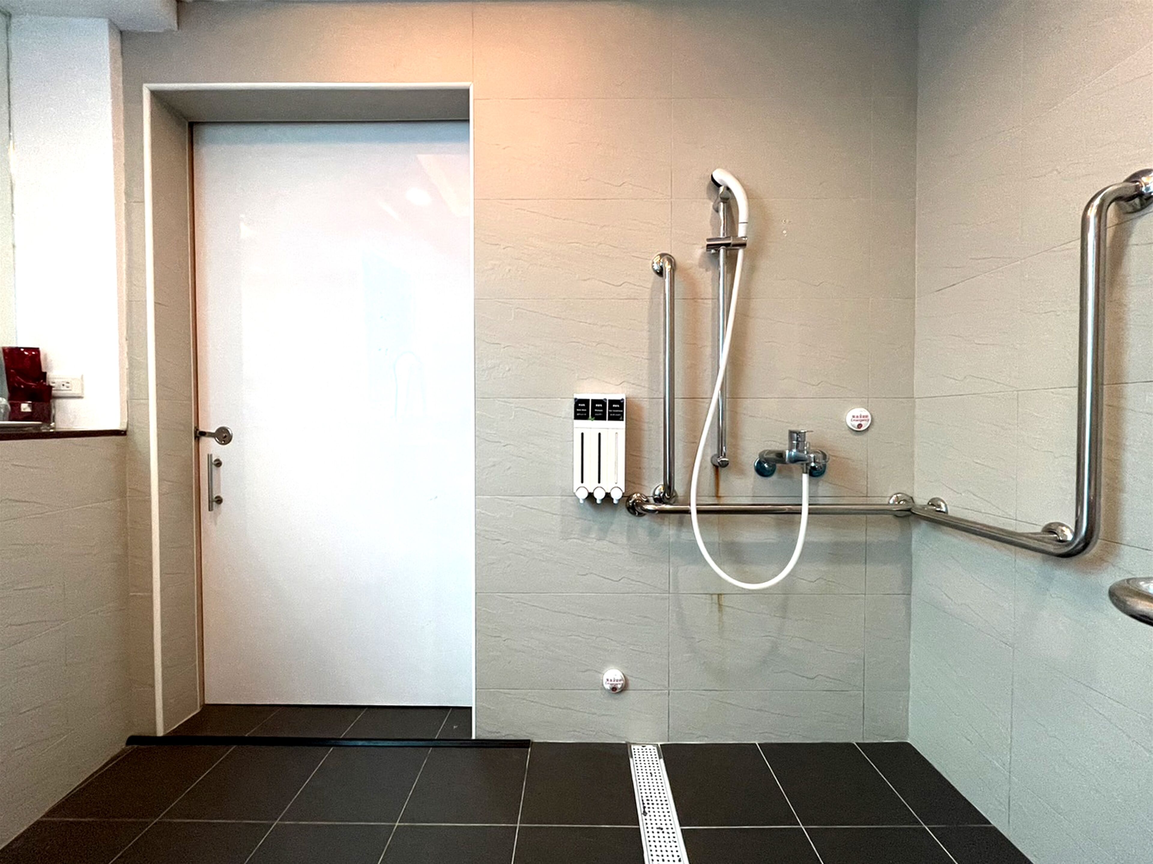 Uma área de chuveiro com porta de vidro, painel de controle e barras de apoio.