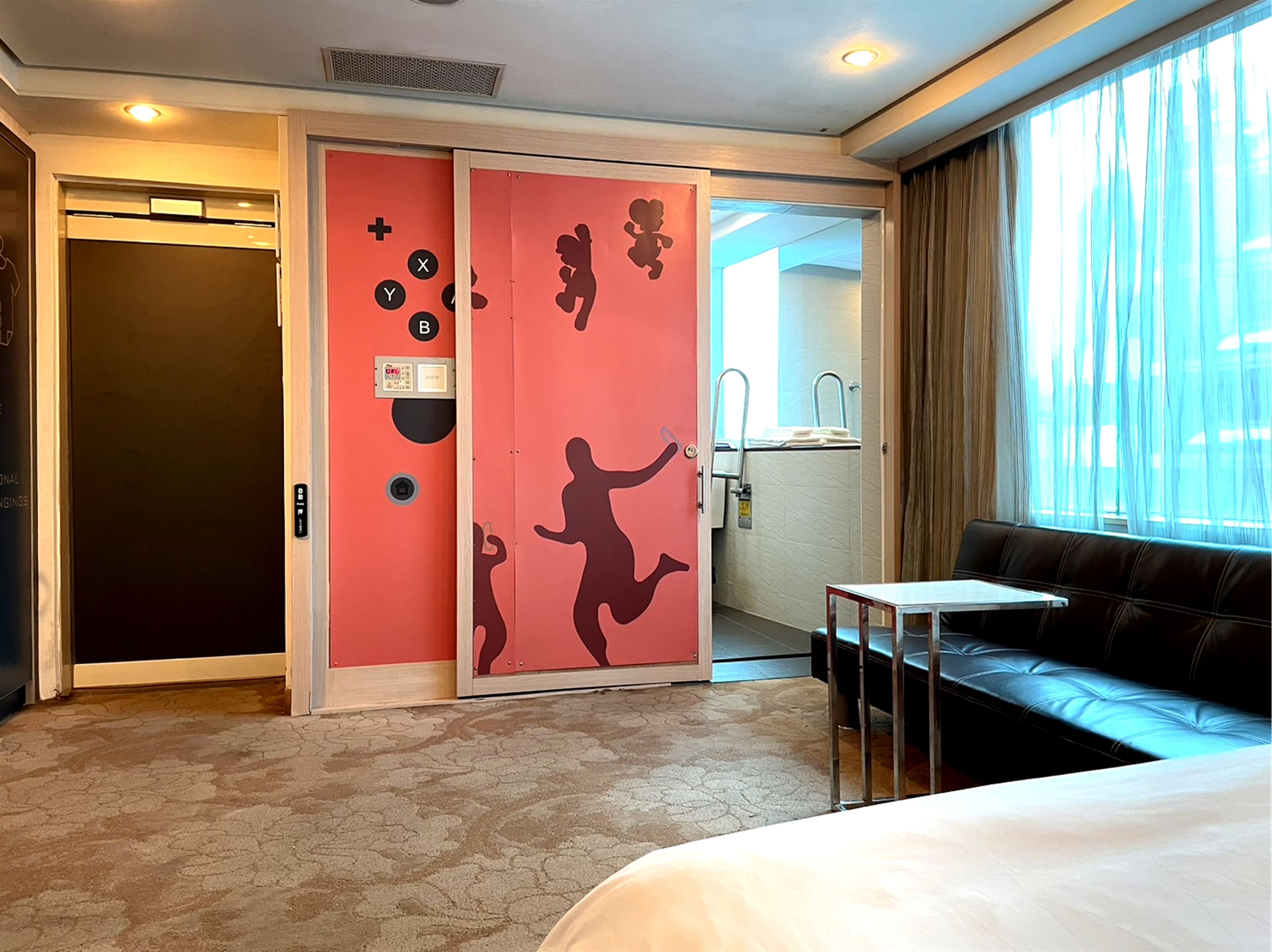 A hotel room with a bed, a sofa, a bathroom with a sink, and a sliding door with a red design.