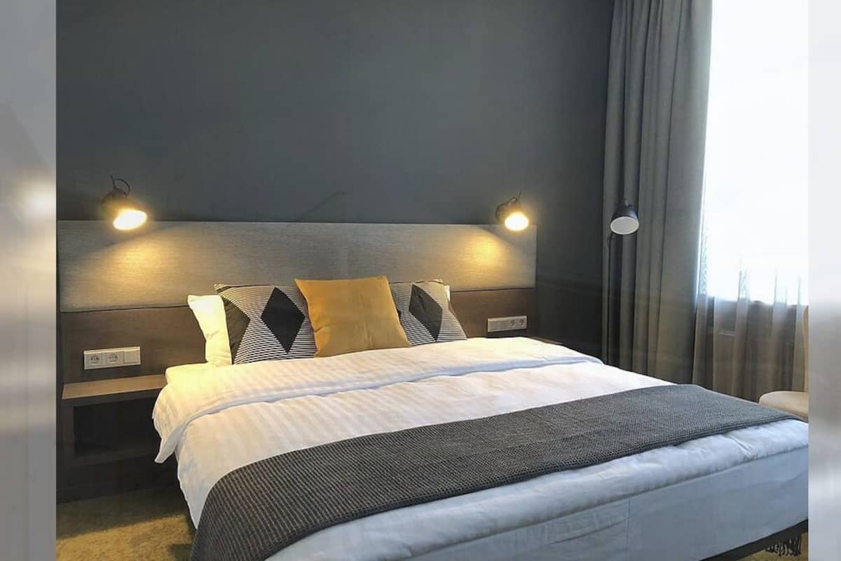Ett modernt hotellrum med en stor säng, en sänggavel med inbyggd belysning, ett sängbord och ett fönster med gardiner.