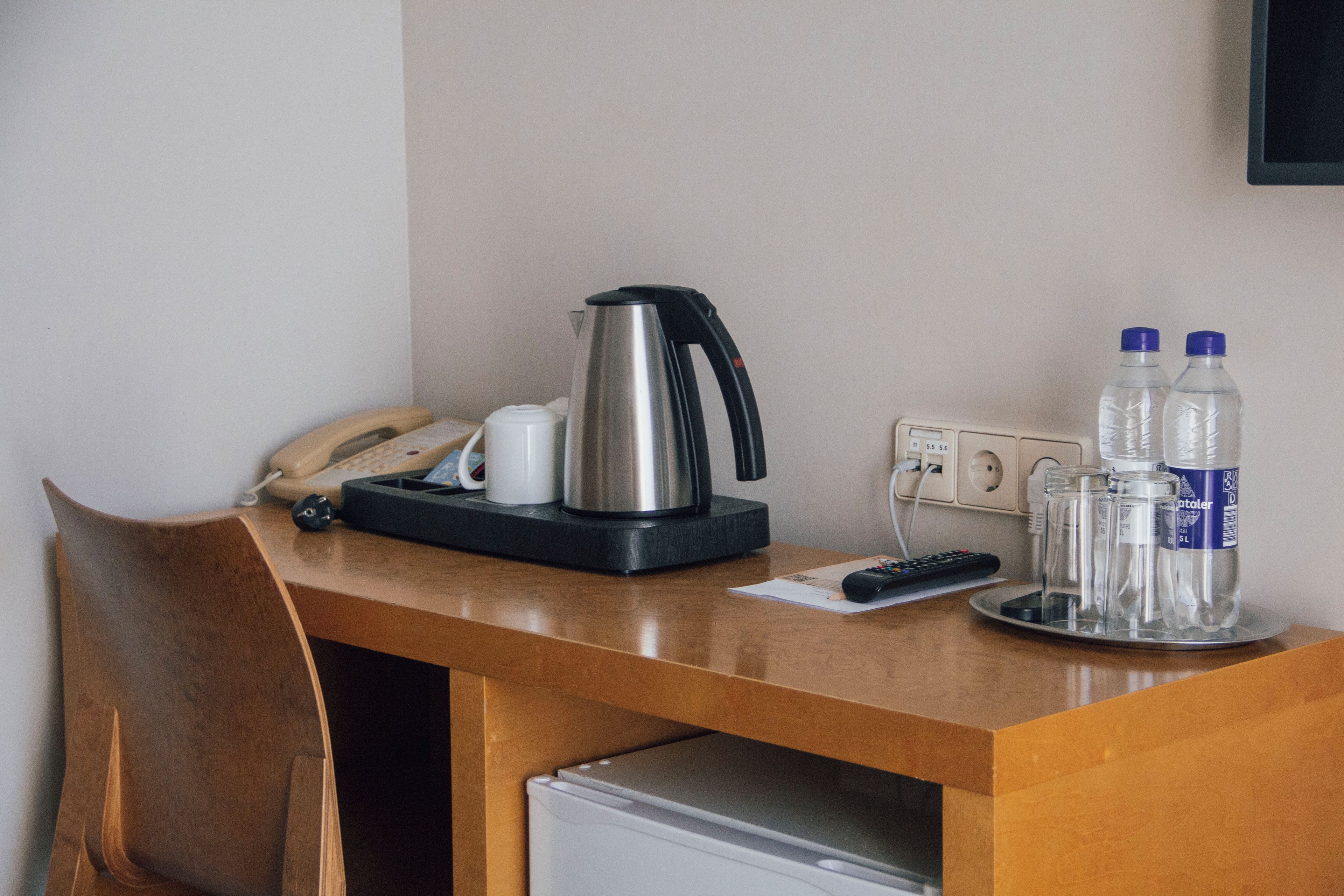 A hotel desk with a telephone, a coffee maker, a remote control, and two water bottles.