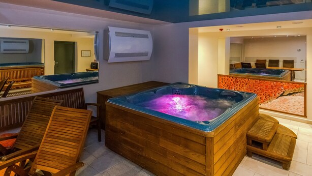 A spa area with wooden loungers, a hot tub, and a massage table. - Hotel Kolumbs (Liepaja)