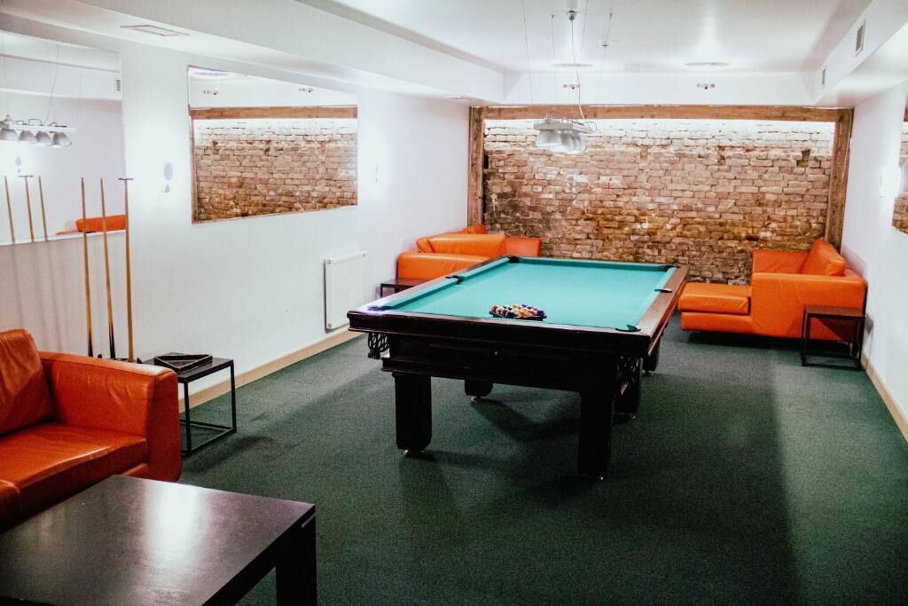 A pool table in a room with brick walls and orange sofas.