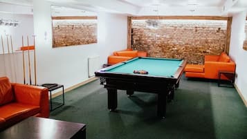A pool table in a room with brick walls and orange sofas.