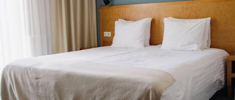 A hotel room with a large bed, a headboard, and a window with curtains.