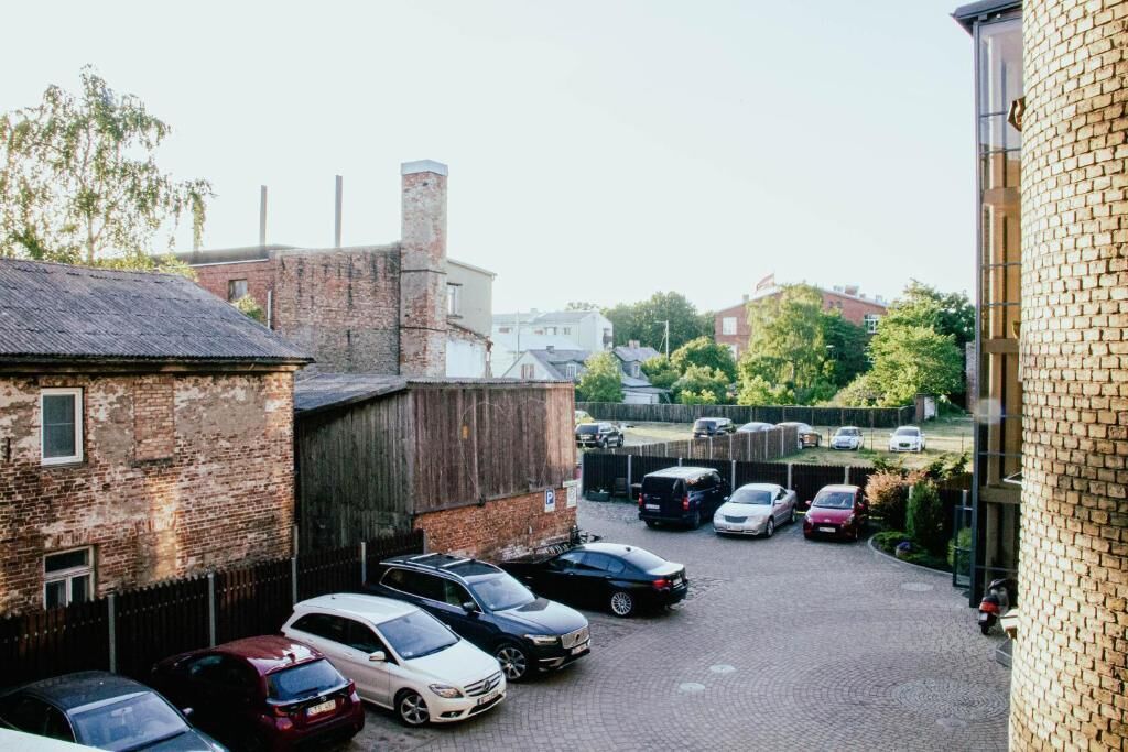 A parking area with multiple cars parked, a brick building, and a fence.