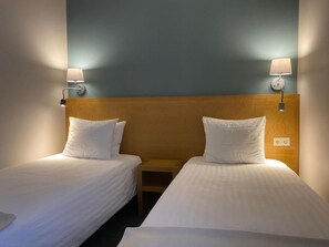 Et hotelværelse med to senge, hver med et træhovedgærde og hvidt sengetøj. Der er vægmonterede lamper på hver side af sengene.