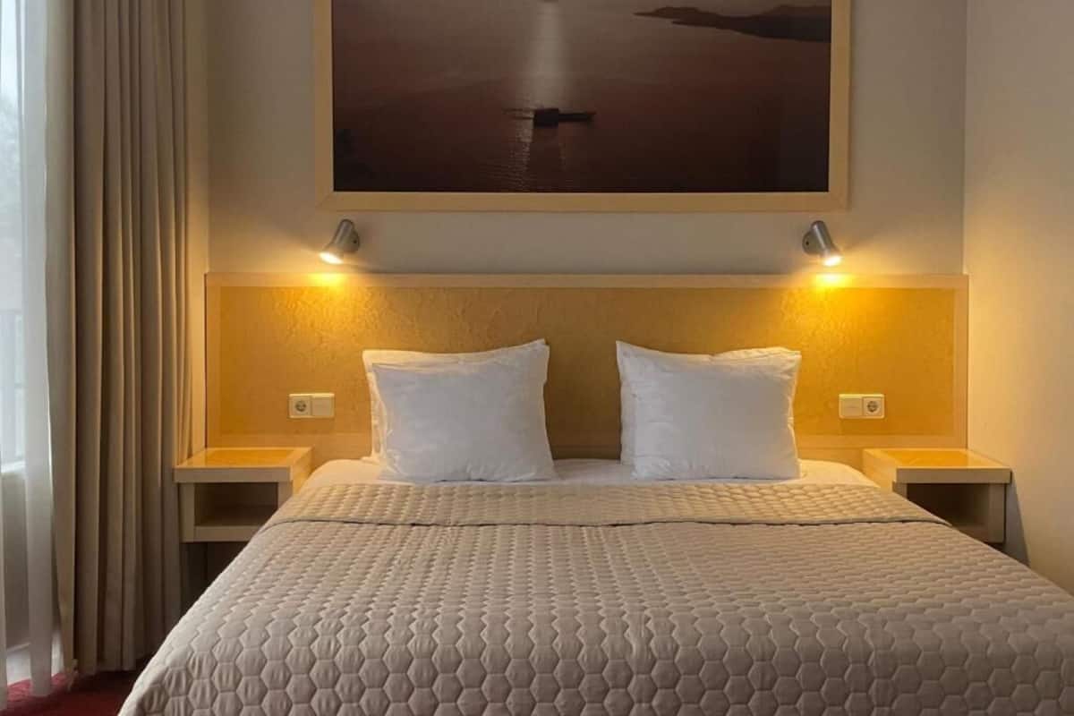 Ett hotellrum med en stor säng, två sängbord, en sänggavel och en tavla som föreställer en båt på vattnet.