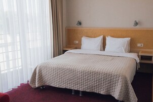 A hotel room with a bed, a headboard, a nightstand, and a window with curtains.