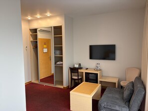 A hotel room with a desk, chair, TV, sofa, and a wardrobe with a mirror. - Hotel Kolumbs (Liepaja)