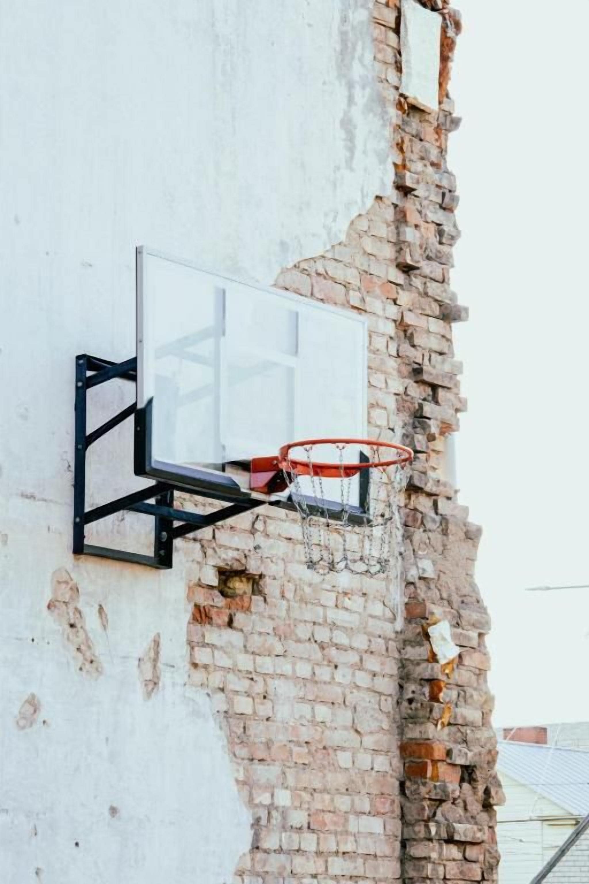 A basketball hoop mounted on a brick wall with visible damage.