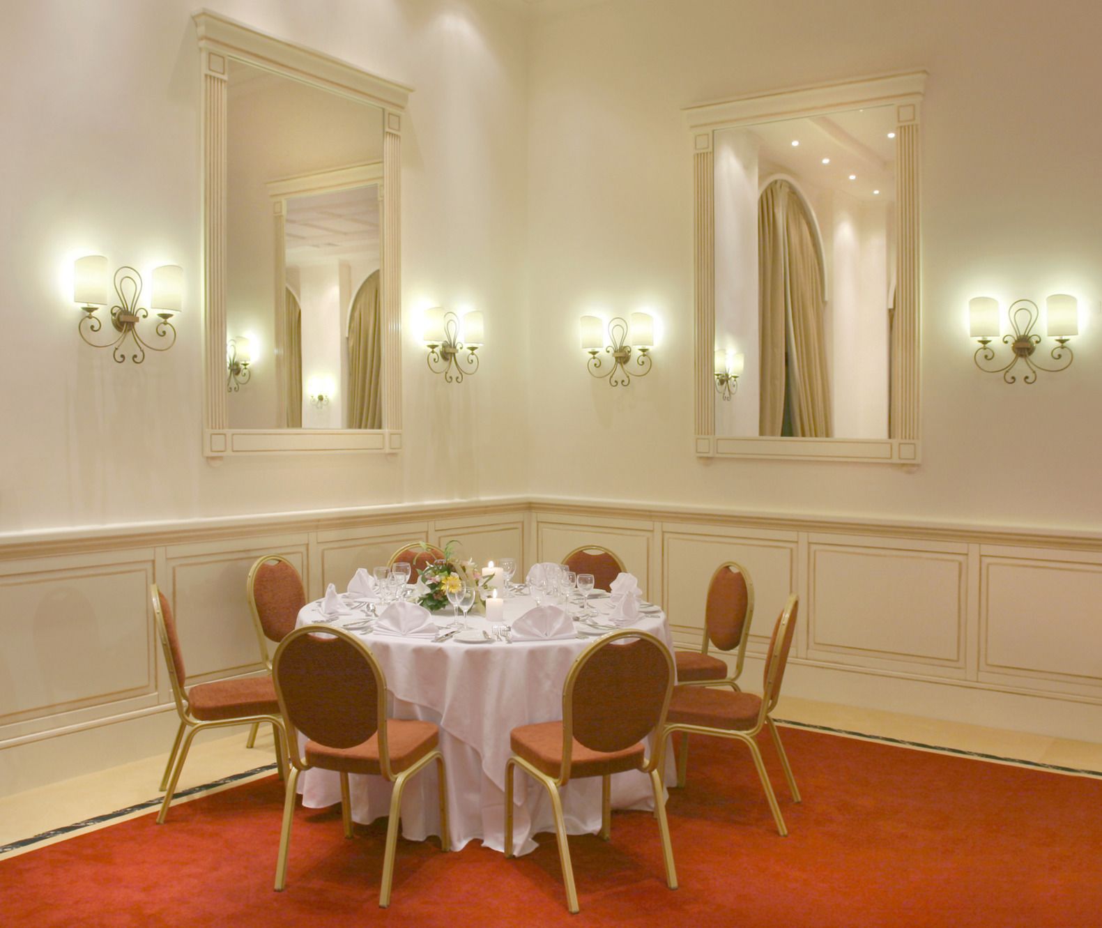 Un comedor formal con una mesa redonda dispuesta para seis comensales, flanqueada por espejos y apliques de pared.