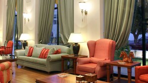 A spacious living area with a sofa, armchairs, and a coffee table. Large windows with curtains are present, and there are wall-mounted lamps. - Volos Palace (Volos)