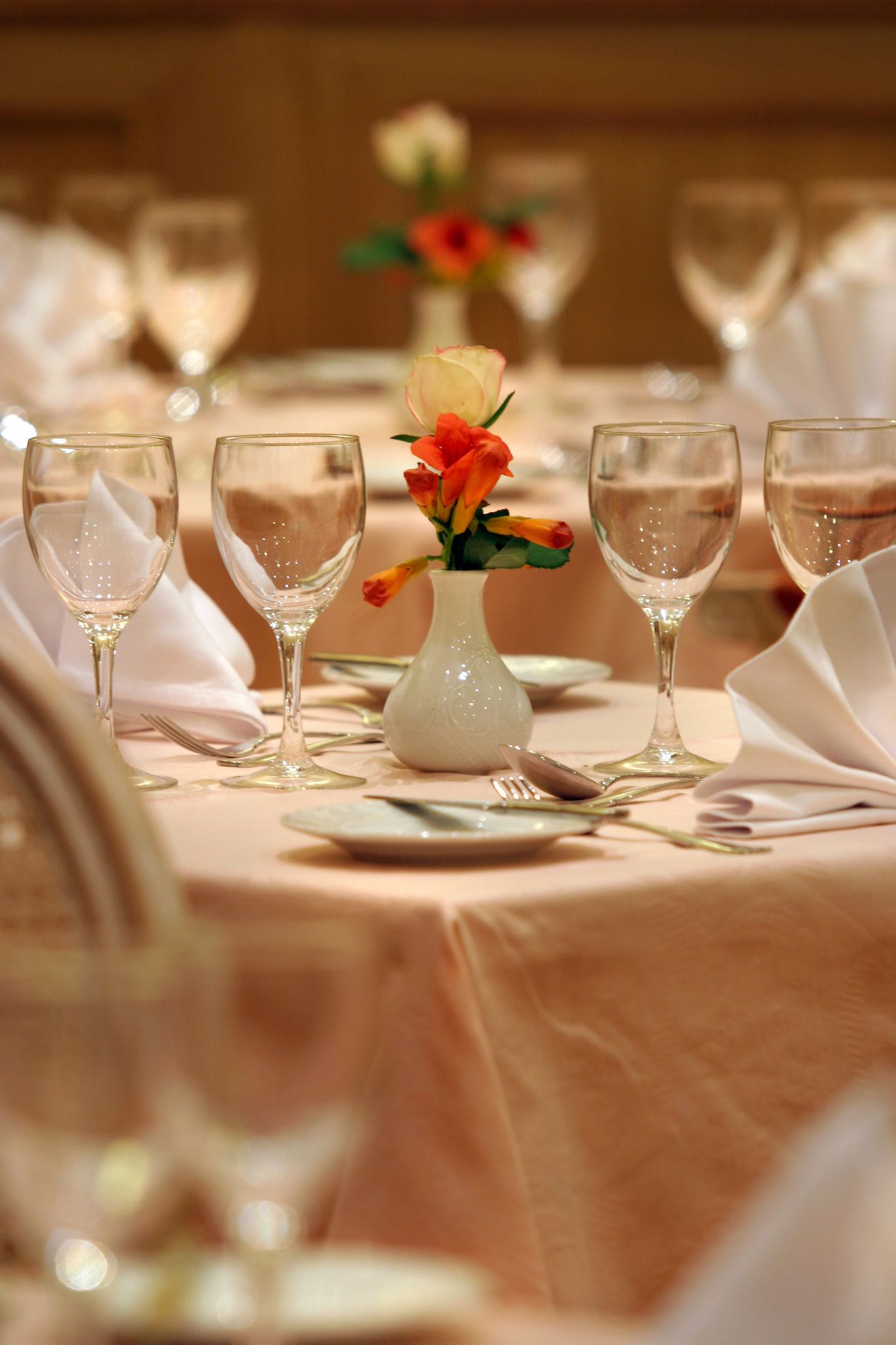 Mesa lista para comer, con copas de vino y un jarrón con flores.