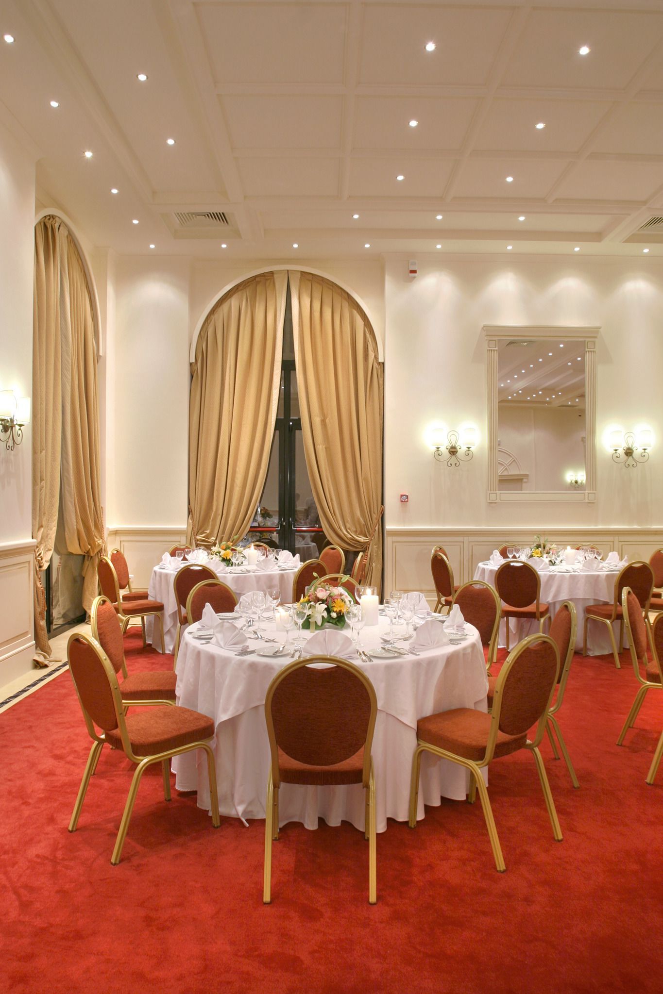 A banquet hall with round tables, red carpet, and gold chairs.
