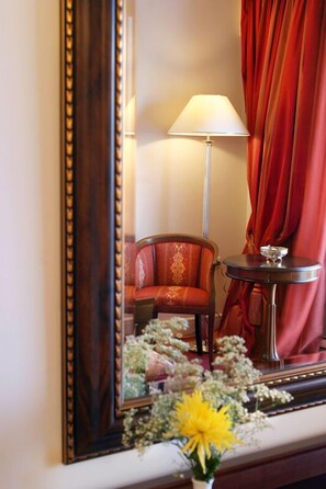 A room with a large mirror, a red chair, a table with a lamp, and a vase with flowers.