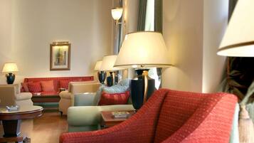 Un hall d’hôtel au design moderne, avec un plafond aux motifs géométriques, plusieurs espaces de détente dotés de meubles rouges et beiges, et des lampes fixées aux murs.