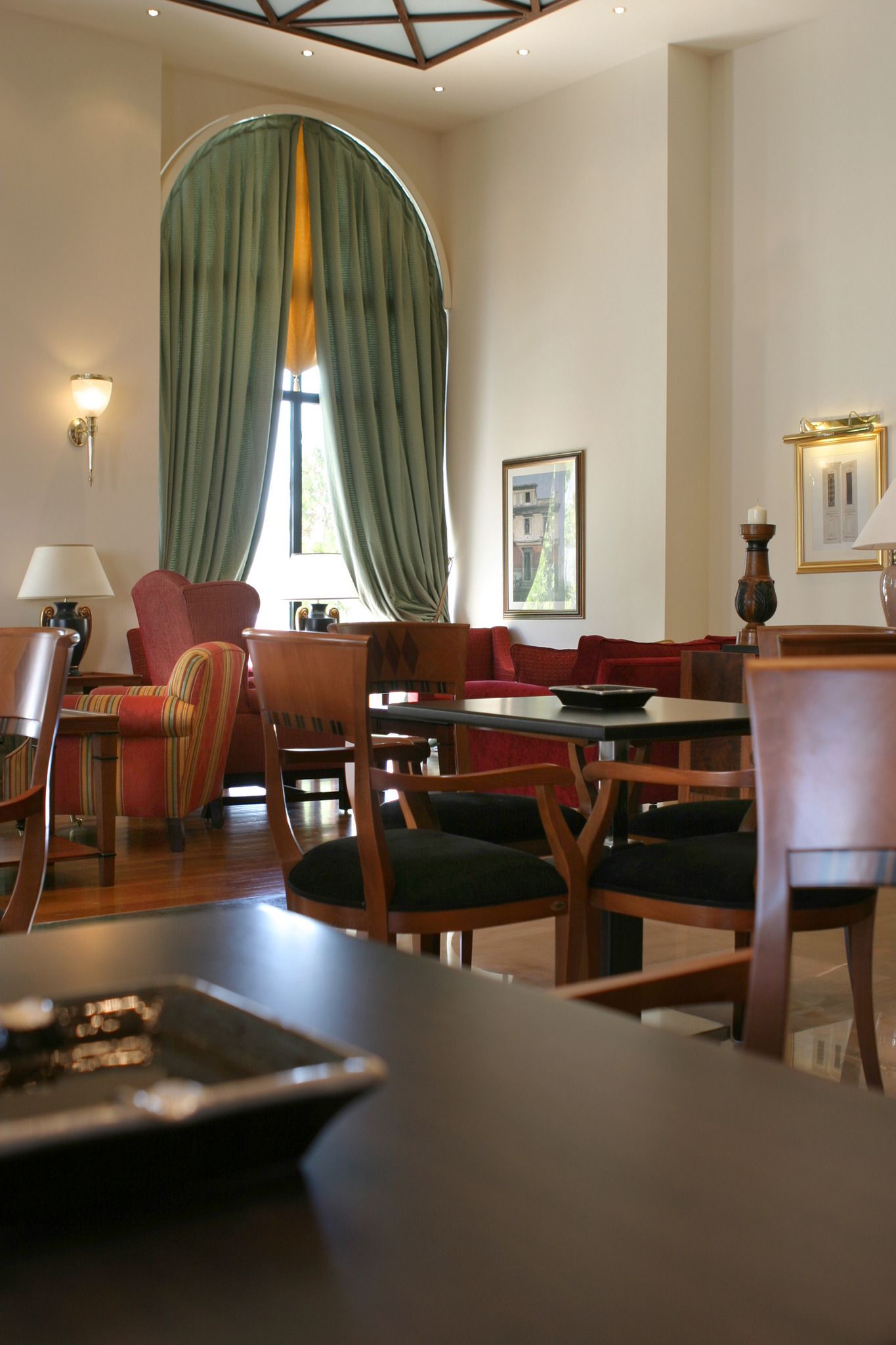 A dining area with wooden furniture, a large window with green curtains, and wall-mounted lamps.