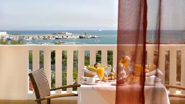 A balcony with a table set for breakfast, overlooking a marina with boats and a distant view of the sea. - Volos Palace (Volos)