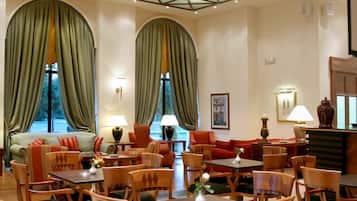 A hotel lobby with a central seating area, multiple tables, and chairs.
