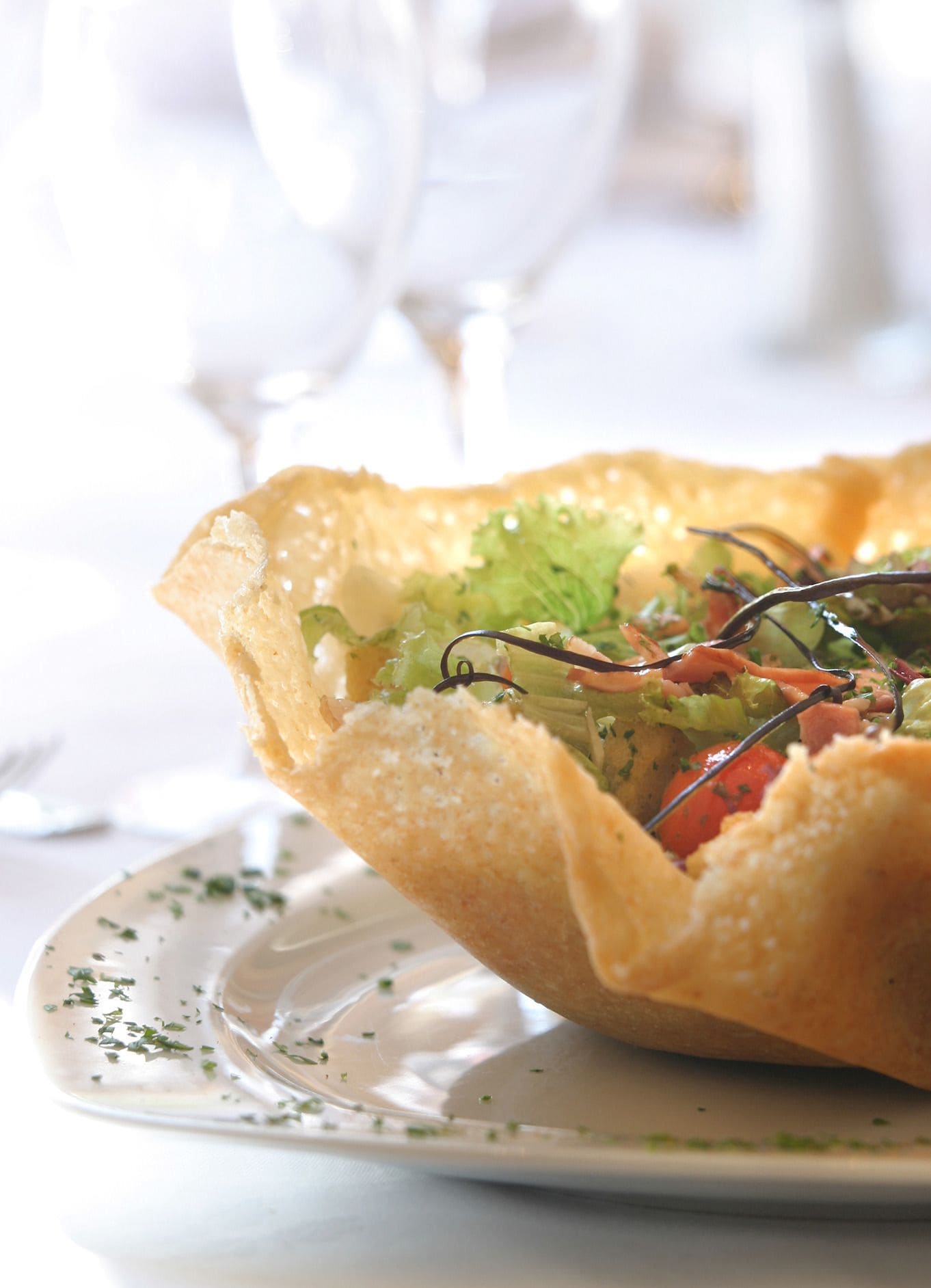 A dish with a crispy, golden-brown crust, possibly a pastry or tart, filled with greens and vegetables, served on a white plate with a fork.