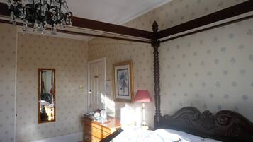 A bedroom with a four-poster bed, a dresser, a mirror, and a chandelier.