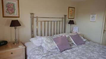 A hotel room with a bed, two bedside lamps, a nightstand, a drawer, a radiator, and two framed floral artworks on the wall.