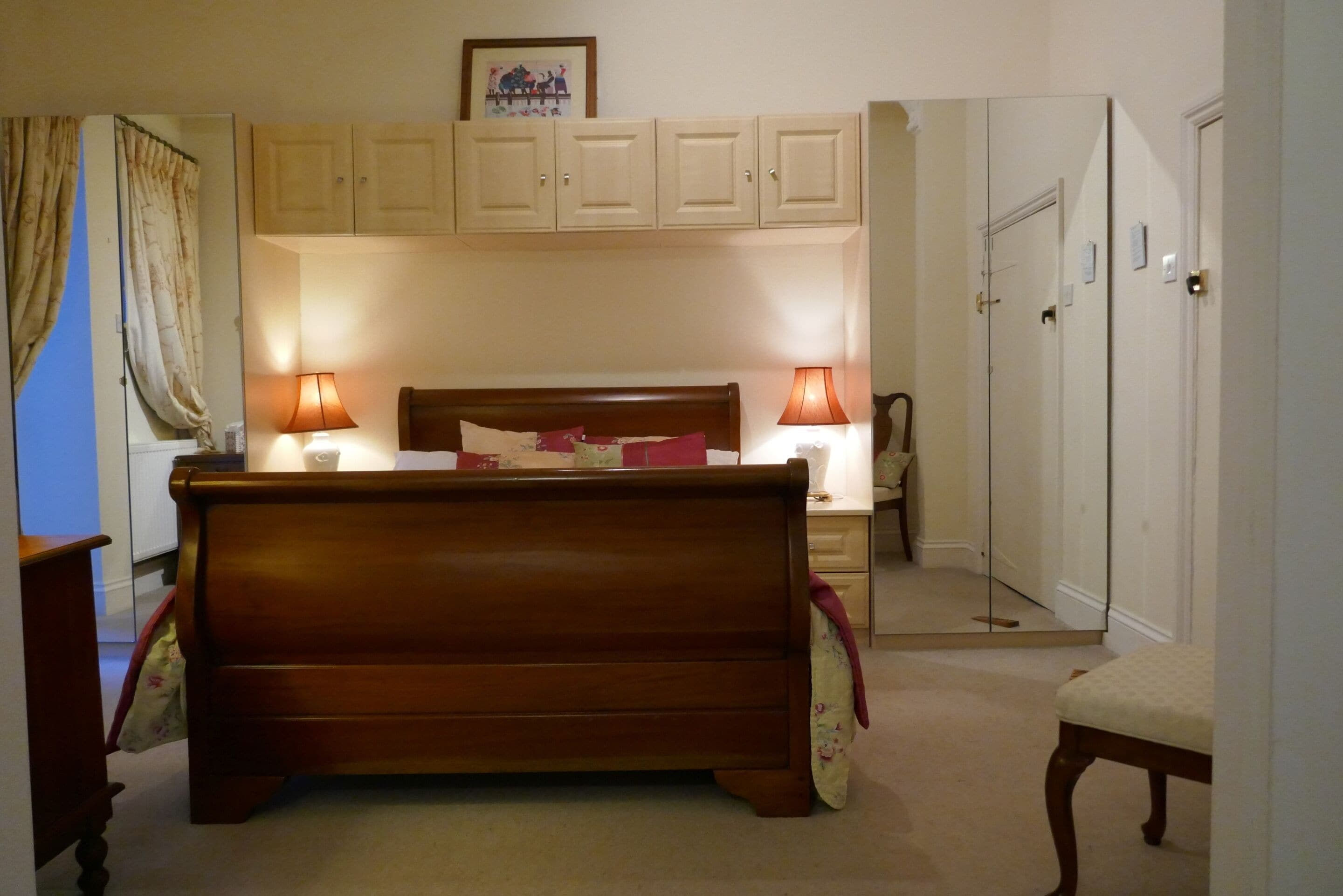 Un dormitorio con una cama de madera, dos lámparas de noche, una mesita de noche, una silla y un armario.