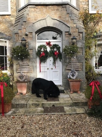 A stone building with a white door adorned with wreaths and red ribbons. Two potted plants with red ribbons are on either side of the door.