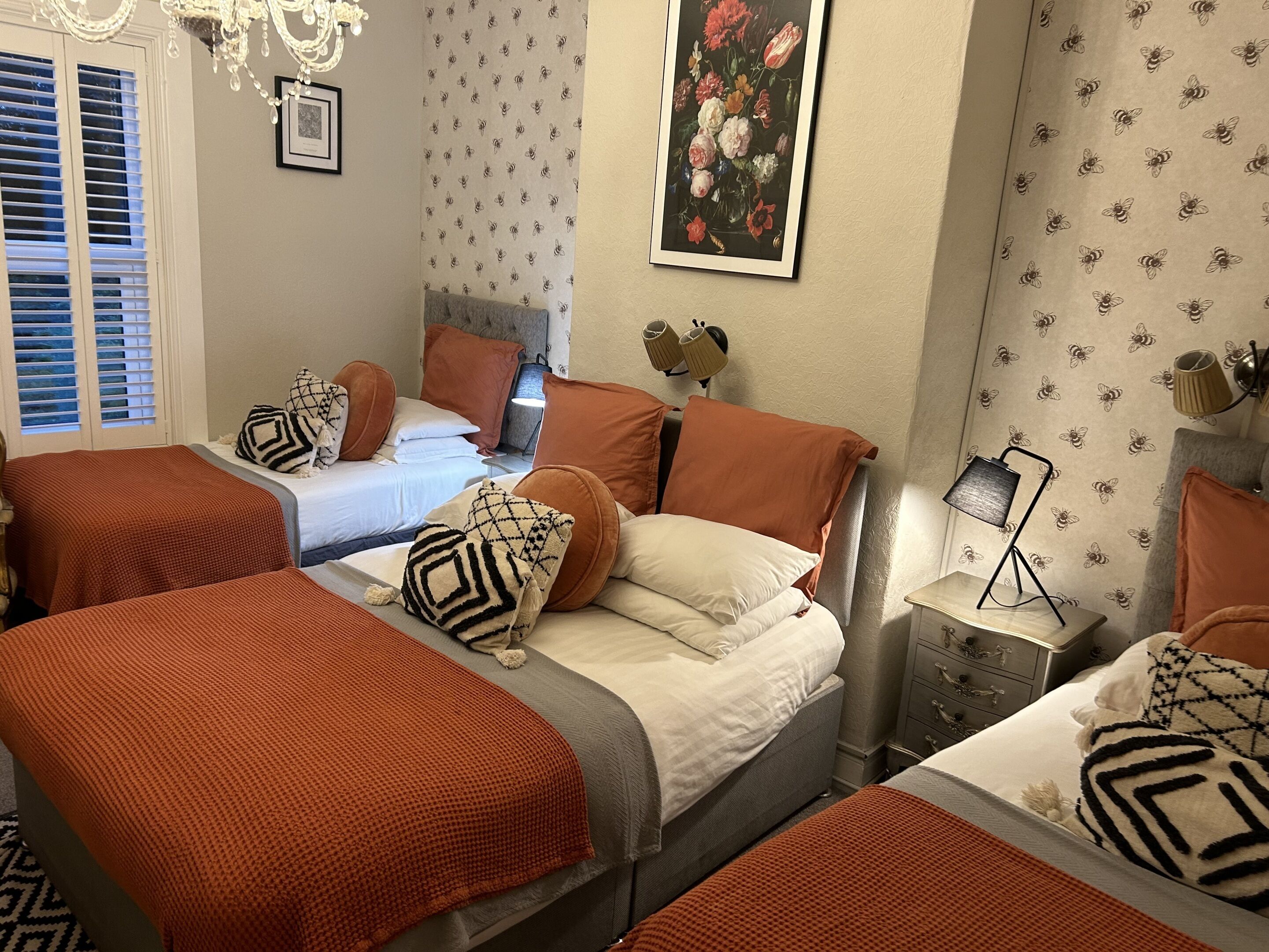 A hotel room with two beds, a chandelier, a painting, and a patterned wallpaper.