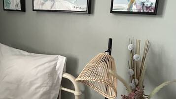 Un dormitorio con una cama blanca, una mesita de noche con una lámpara y un jarrón de flores, y pinturas abstractas en la pared.