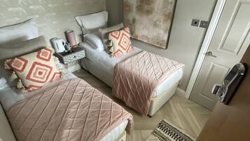 Un dormitorio con dos camas, una mesita de noche con lámpara, un cuadro en la pared y una puerta.