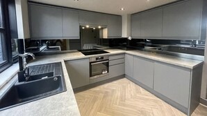 A modern kitchen with grey cabinets, a black sink, and a herringbone wood floor. - Maison Claire (Chester)