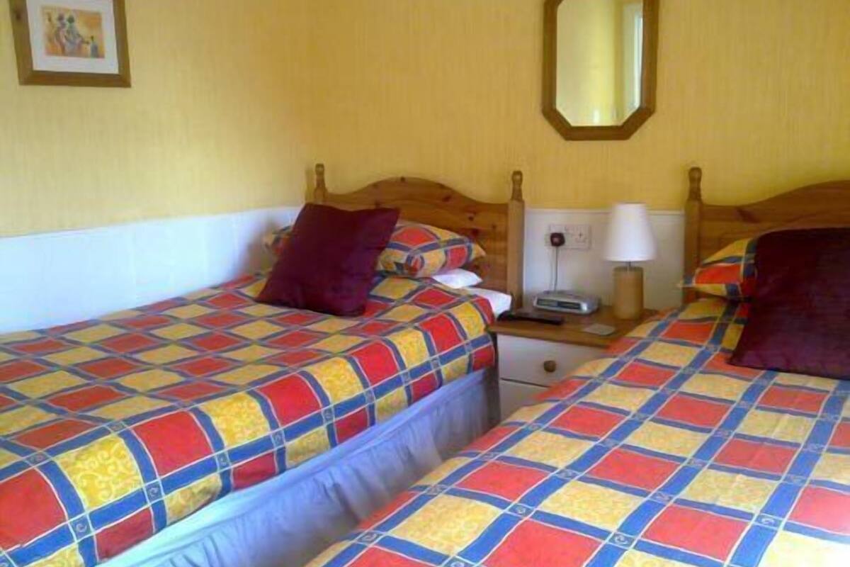 Quarto com duas camas, cada uma com um colcha colorida, uma cabeceira de madeira, mesa de cabeceira com abajur e um espelho na parede.