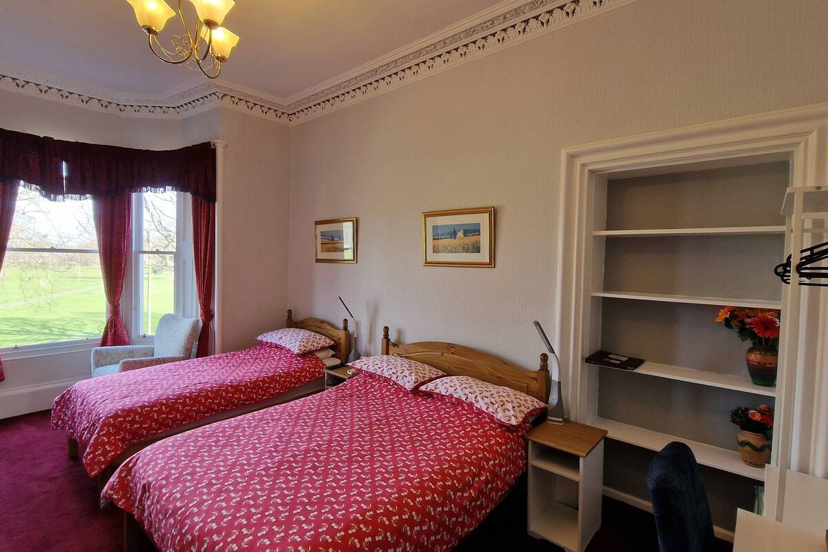 Quarto com duas camas, televisão, escrivaninha e guarda-roupa.