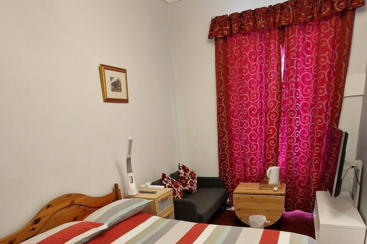 Quarto com cama, mesa de cabeceira, cômoda, cadeira e janela com cortinas.