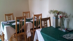 A dining area with wooden chairs and tables covered with green and white tablecloths. There are framed pictures on the wall and a vase with flowers on the table. - Mackenzie Guest House (Edinburgh)