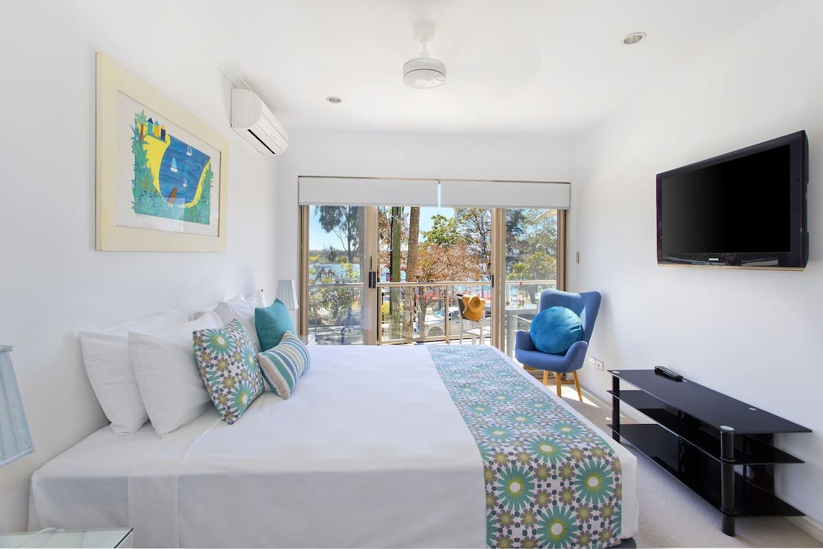 A bedroom with a bed, a TV, a chair, and a balcony with a view.