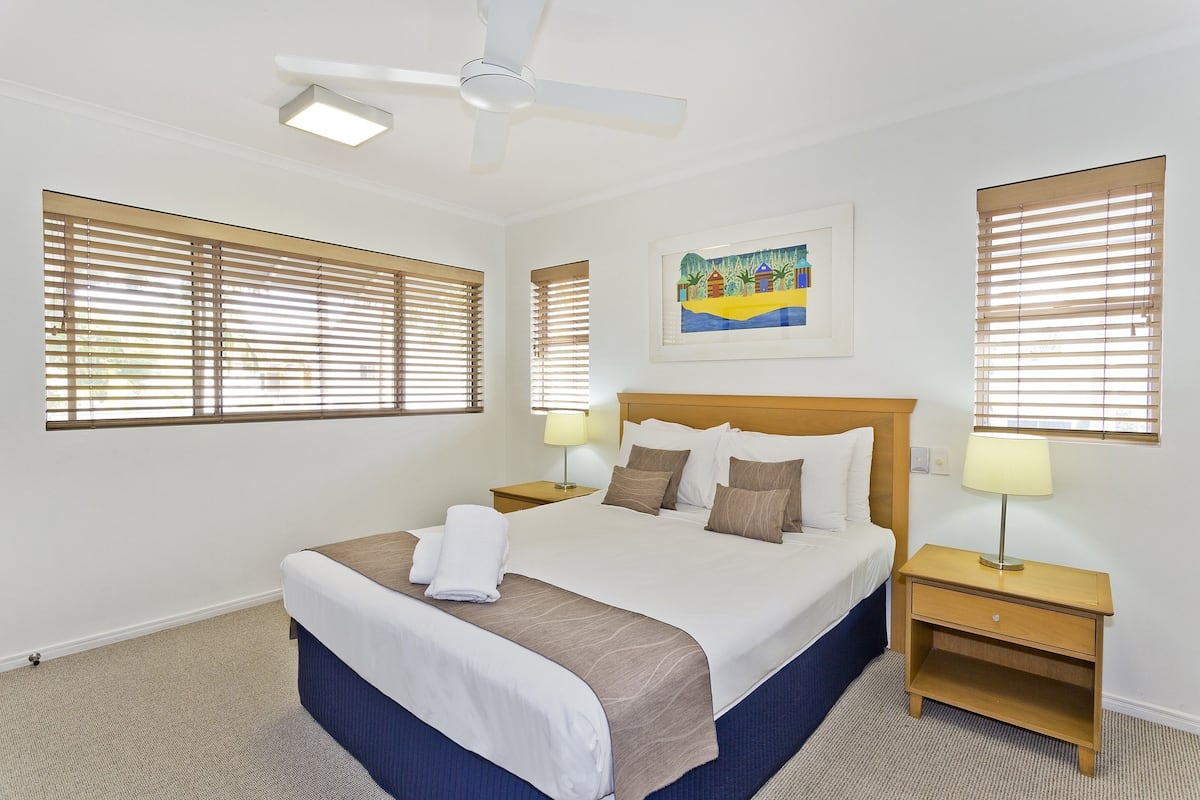 A hotel room with a large bed, two bedside tables with lamps, a ceiling fan, and a painting on the wall.