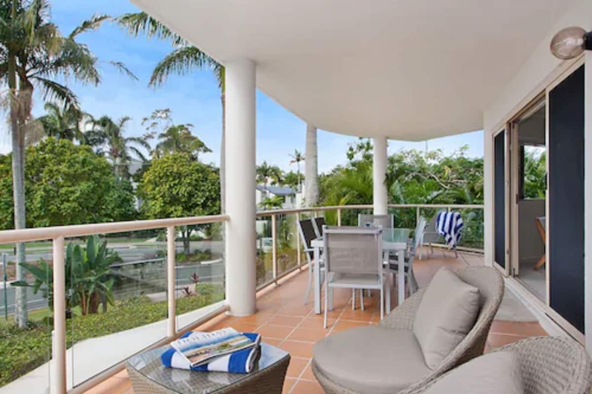 A balcony with a glass railing, outdoor furniture, and a view of greenery.