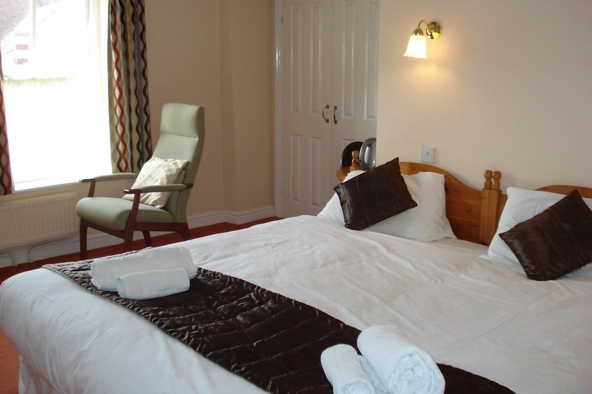 Habitación de hotel con cama, una silla, armario y ventana con cortinas.
