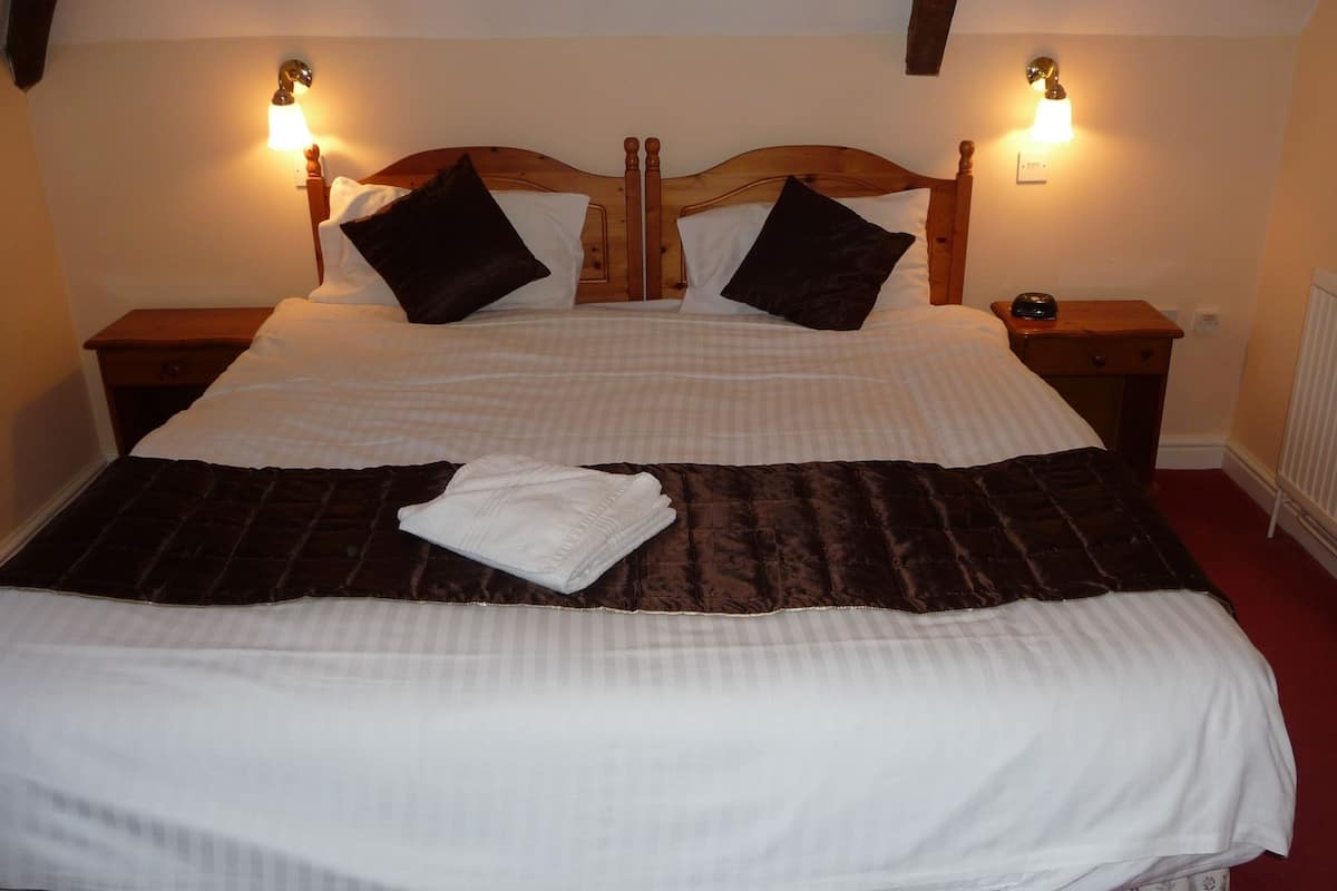A double bed with a brown quilt, two nightstands, and a white radiator.