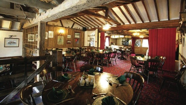 A restaurant with wooden beams, multiple dining tables, and chairs.