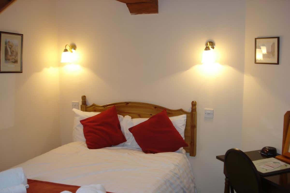 A neatly made bed with red pillows, a wooden headboard, and two wall-mounted lights.