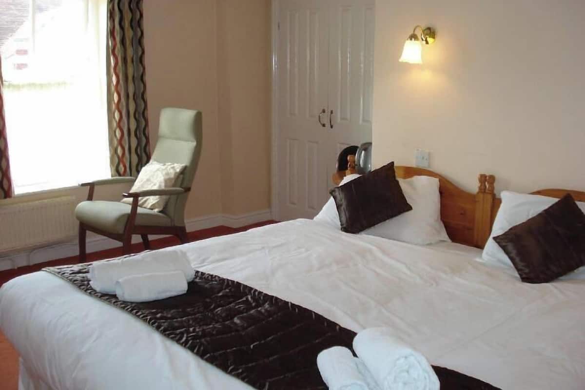 A hotel room with a bed, a chair, a wardrobe, and a window with curtains.
