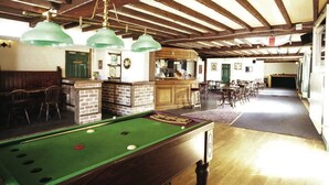 A billiards table with a green felt surface, wooden pool cues, and a green felt pocket. There are two green pendant lights hanging from the ceiling.