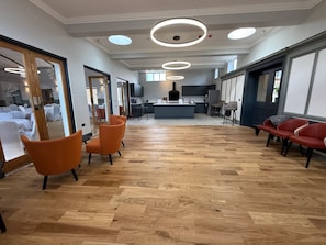 Une pièce spacieuse avec un plancher en bois, des chaises orange, un coin cuisine et une grande fenêtre.