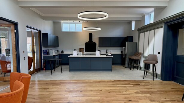 A modern kitchen with a central island, dark cabinetry, and a large window.