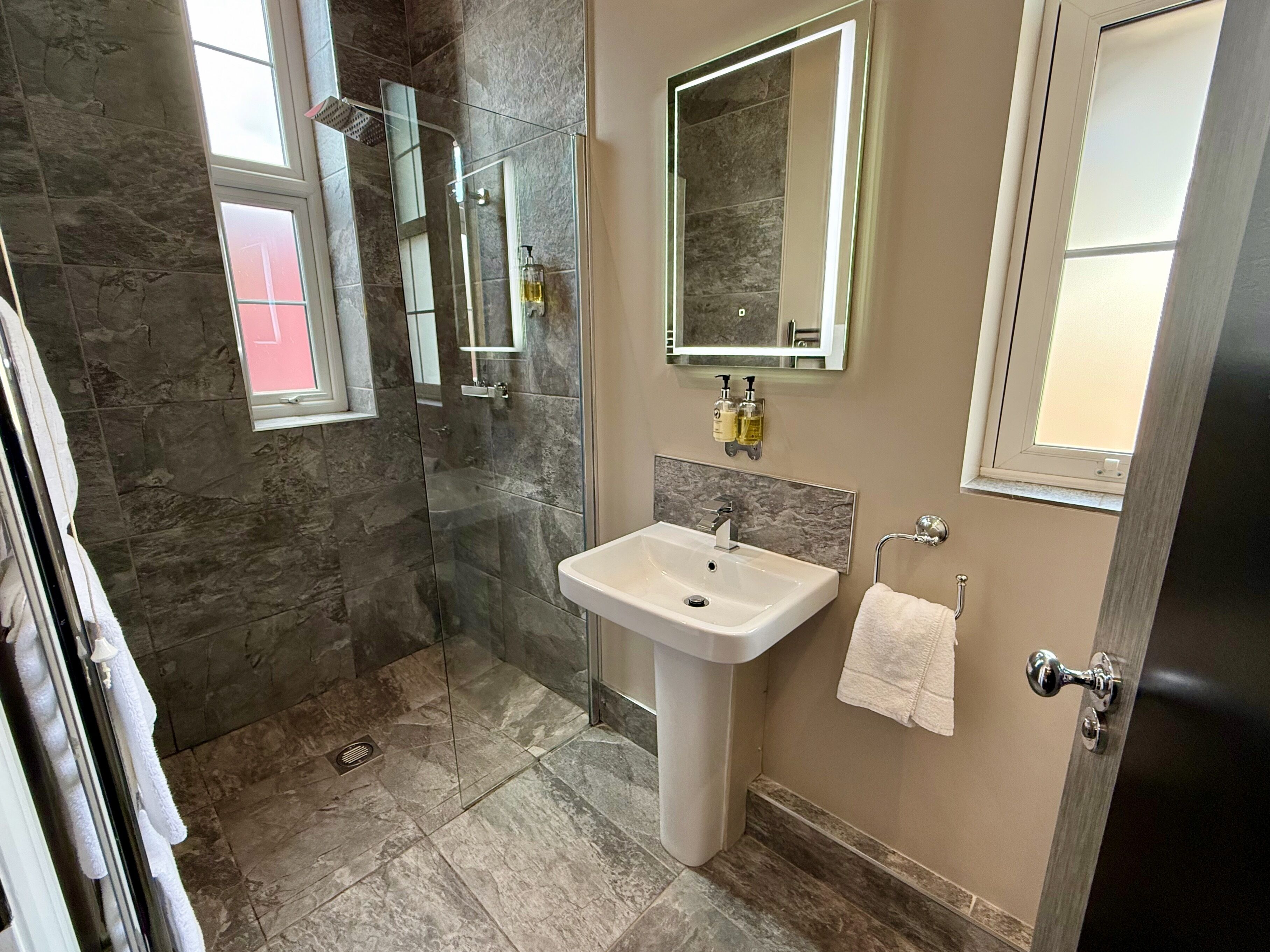 A bathroom with a glass shower enclosure, a sink with a mirror above it, and a towel hanging on the wall.