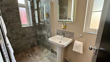 A bathroom with a glass shower enclosure, a sink with a mirror above it, and a towel hanging on the wall.